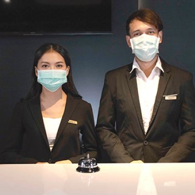 A woman and a man wearing dark suits standing behind a counter in masks